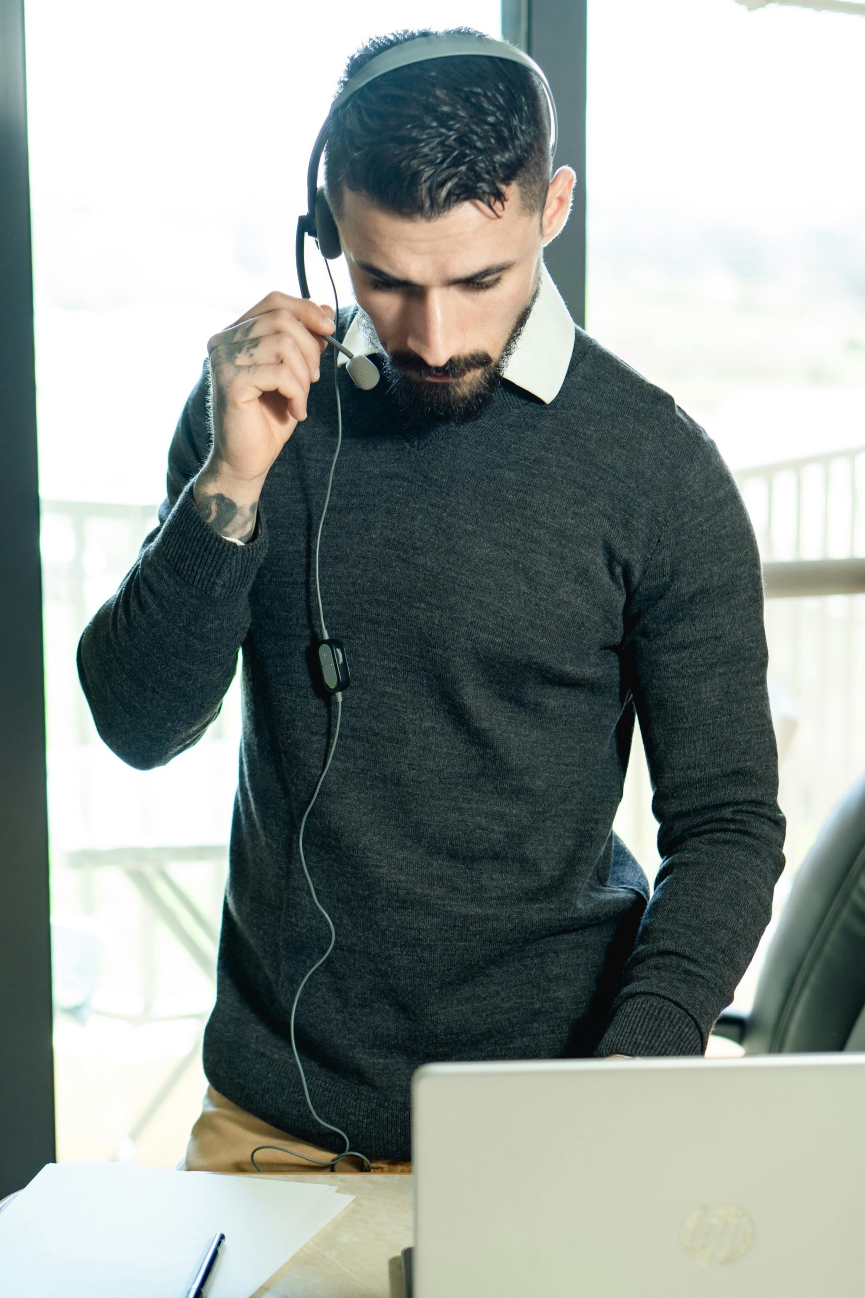 A bearded man in a home office setting uses a headset and laptop, conveying modern work tactics.